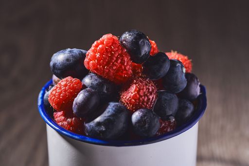 A horizontal shot of washed raspberries and blueberries in a ceramic cup on a blurred background