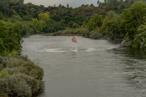 A view of a bucket dipping water to fight a fire, hanging from a helicopter