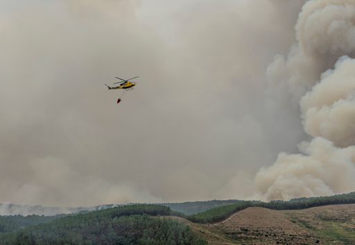 A view of a bucket dipping water to fight a fire, hanging from a helicopter against smoke