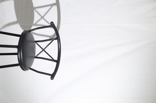 A vertical shot of an empty black chair in a studio with a reflection on white background