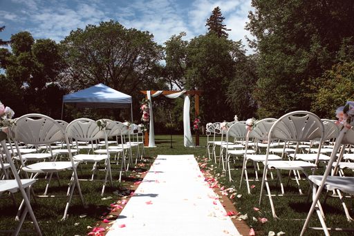 An outdoor wedding venue with an aisle with floral petals and white chairs in a park