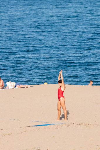 A woman in a red swimsuit stretching before playing beach volleyball