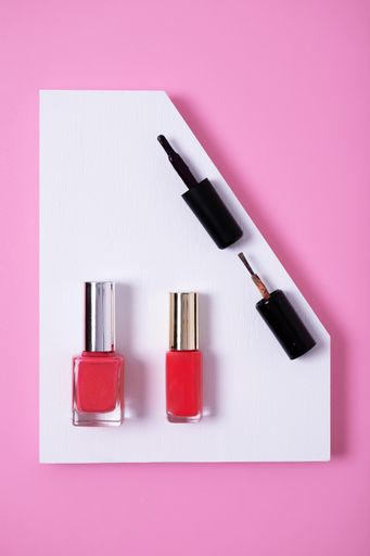 A vertical high angle shot of pink nail polishes on a multicolor paper