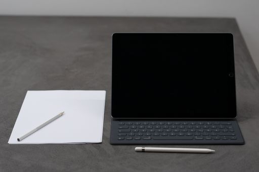 A closeup of a white tablet with portable keyboard, a piece of white paper with a pen and pencil