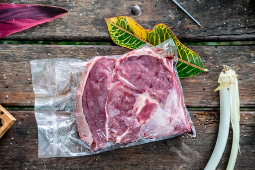 A top view of a raw red steak in a plastic bag on a picnic table
