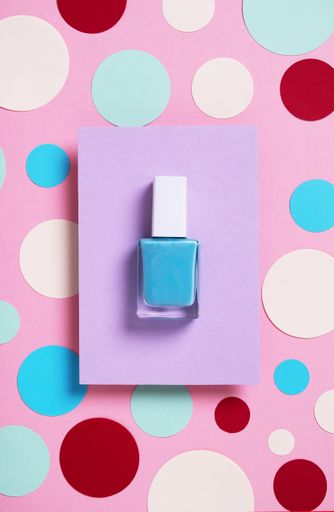 A vertical high angle shot of blue nail polish on a multicolor paper