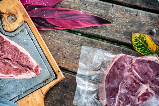 A top view of a board with steak slice and a steak in plastic bag on a wooden table