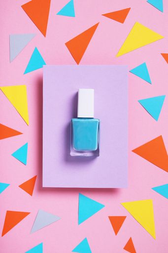 A vertical high angle shot of blue nail polish on a multicolor paper
