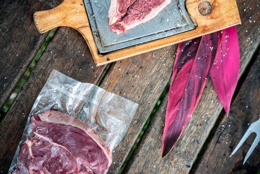 A top view of a board with steak slice and a steak in plastic bag on a wooden table