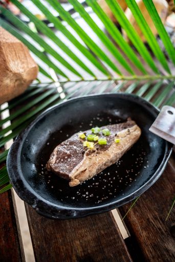 A vertical shot of a steak cooking in a black pan with spring onion slices