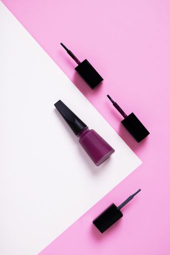A vertical high angle shot of purple nail polish on a multicolor paper