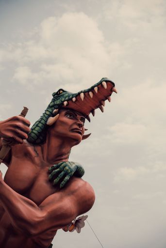 A low angle shot of a man wax figure with a crocodile against a cloudy sky in an amusement park