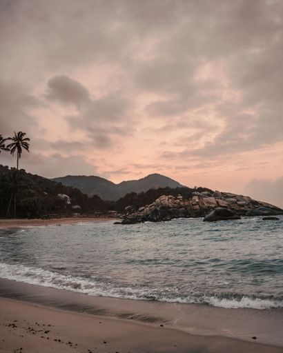 Cloudy sunset sky over wavy sea, rocks, and sandy beach. Heaven on Earth