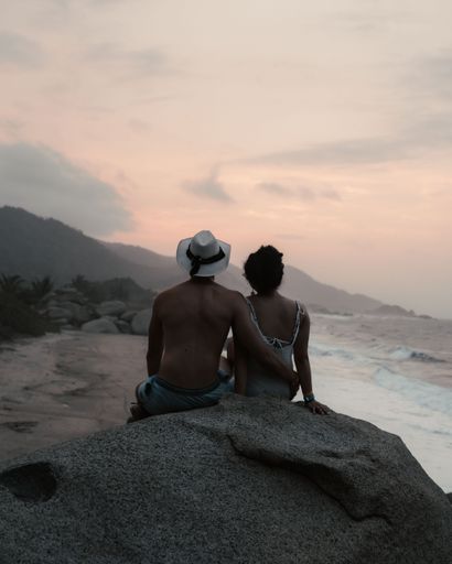 A couple sitting on the heap of sand on the beach with wavy sa at scenic sunset