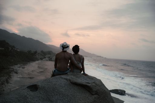 A couple sitting on the rock by the sea shore enjoying the twilight