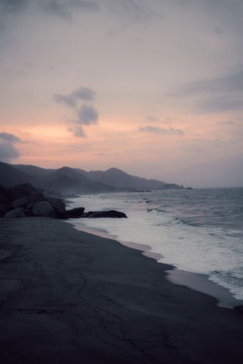 A vertical shot of ocean waves reaching the shore in a cloudy relaxing weather