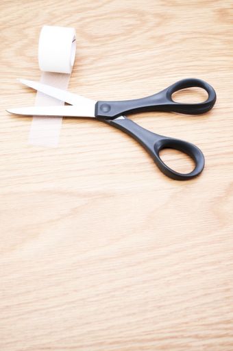 pair of scissors and transparent adhesive tape on a wooden background with copy space
