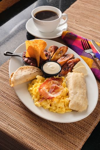 A vertical closeup shot of a typical breakfast with fried plantains, tortilla, eggs and bacon