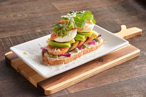 A closeup shot of Italian bruschetta with tomatoes, avocado, poached eggs, and onions arugula