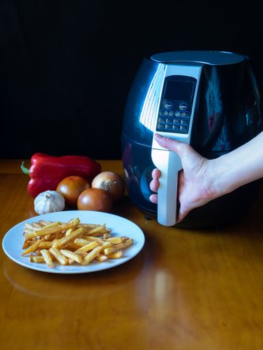 A vertical shot of a female hand opening a hand fryer to prepare french fries and vegetables
