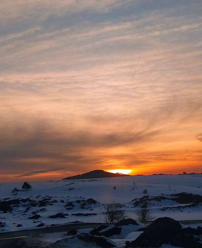 A beautiful view of the sunset over a snowy land under a cloudy sky