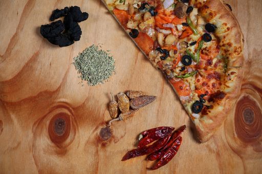 A top view of freshly made tasty pizza with spices and other ingredients on wooden table