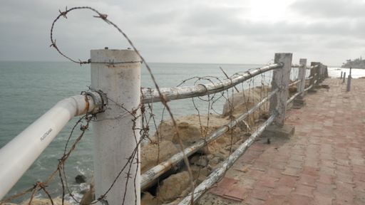 A side shot of a barbed fence on a sideroad looking over a sea in daylight under the cloudy sky