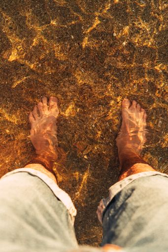 A high angle shot of a man wearing jean shorts standing on the beach with his feet in the water