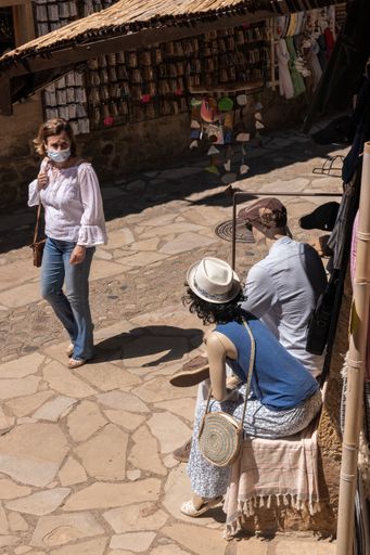 A masked woman walking along the streets of the coast on a summer day passes in front of a store with two sitting mannequins