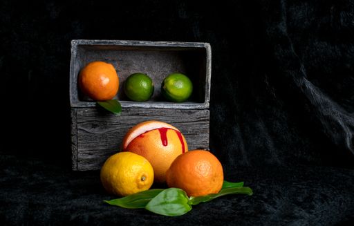 A still life with green leaves and citrus fruits in a wooden box on a dark background