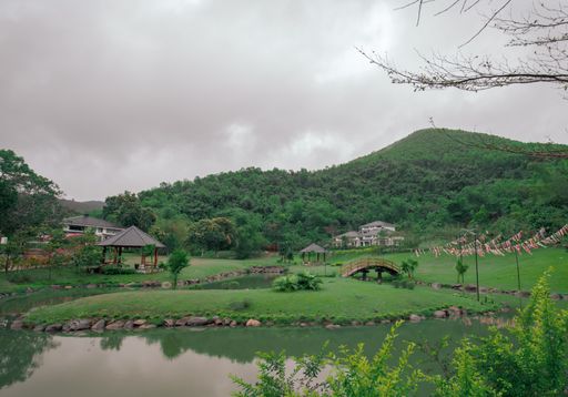 A view of a beautiful green area with pavillions and hills and a pond in the middle