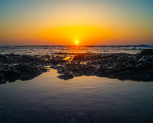 A scenic view from the beach with rocks and transparent water to the beautiful sunset
