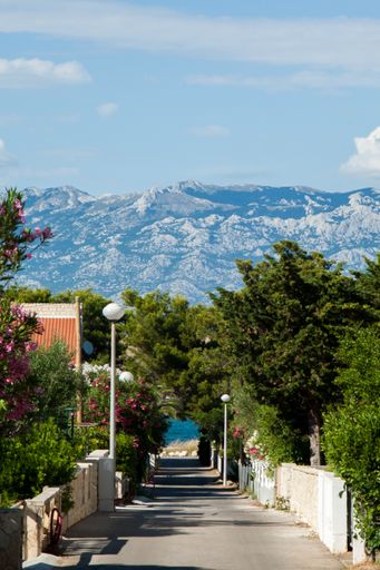 An alley towards the sea on the island of Vir, Croatia. Scenic mountains in the background