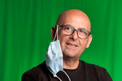 A closeup of a bald male with glasses and medical mask against a green wall
