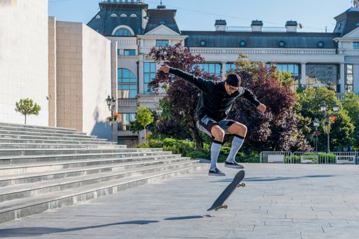 A young male in shorts doing a skateboard trick near a building