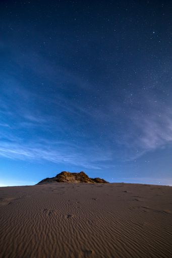 A vertical shot of a desert dune on a beautiful starry night sky