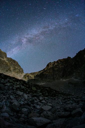 A vertical shot of a starry night sky with mountains and rocks in the foreground