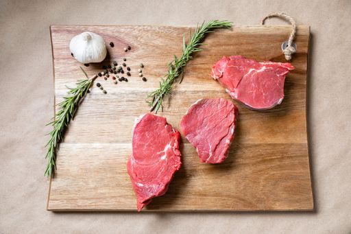 A top view shot of slices of raw meat on a wooden board with spices