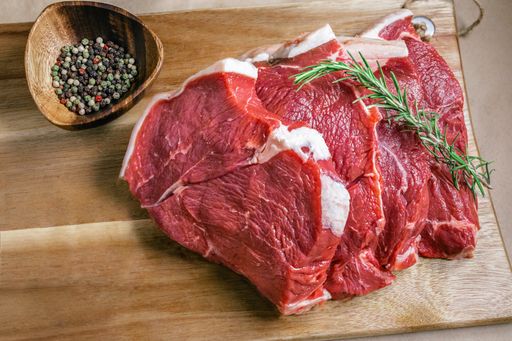 A top view shot of slices of raw meat on a wooden board with spices