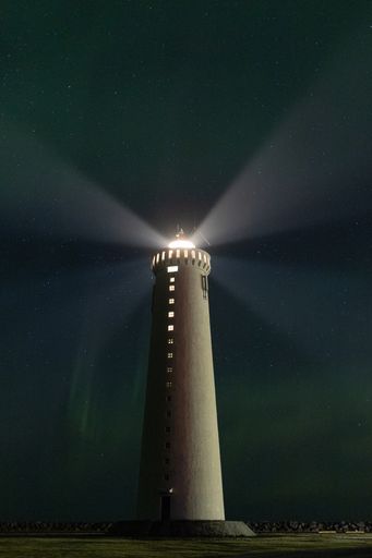 An outdoor view of the Gardur lighthouse against the beautiful aurora borealis sky in Iceland