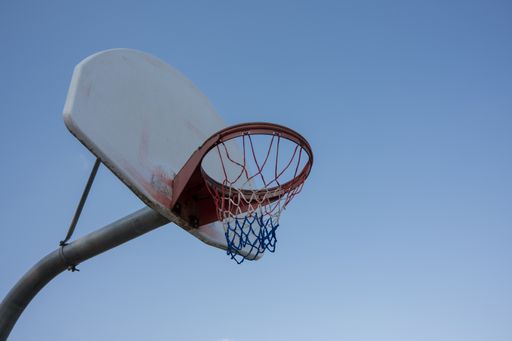 A low-angle shot of a basketball hoop against the blue sky in the playground