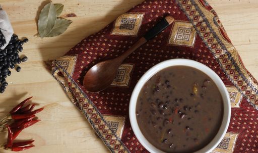 A top view of Black Bean Chili on a wooden table with spices and dried black beans