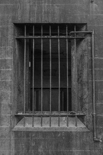 A grayscale shot of a an open window with metal bars on it in an old abandoned building