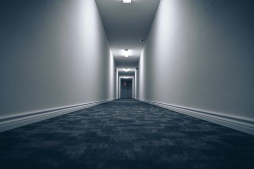 A long hallway with blue carpet and white walls with lighting lamps on the ceiling