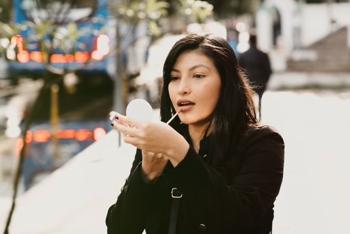 A young Hispanic brunette female applying lipstick in the street