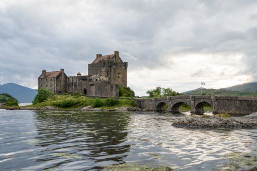 View of Eilean Donan Castle, Scotland, United Kingdom with a river and stone bridge on a cloudy day
