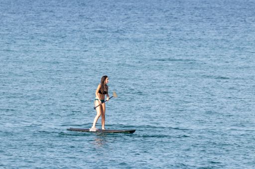 A young female in bikini paddle surfing on the beach in Pals on a sunny summer day