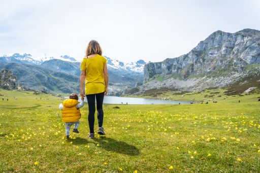 A back shot of a child taking his first steps with his mother in a green field near to Lake Ercina, Lakes of Covadonga, Asturias, Spain