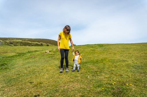 A Caucasian child taking his first steps with his mother in a green field near to Lake Ercina, Lakes of Covadonga, Asturias, Spain