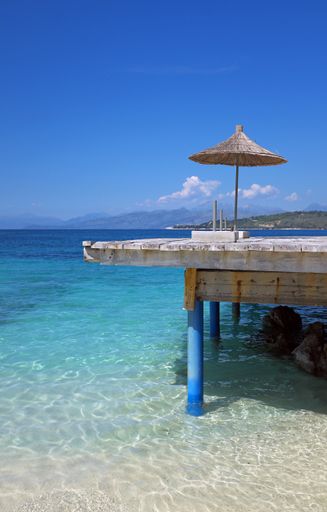 A vertical shot of a wooden dock with a beach umbrella on the coast of Sarande, Albania